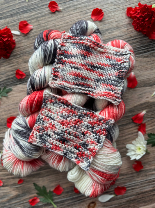 Knitted swatches on skeins of yarn with red and white flowers on a wooden surface