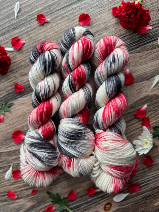 Three skeins of multicolored yarn on a wooden surface with red flowers and petals.